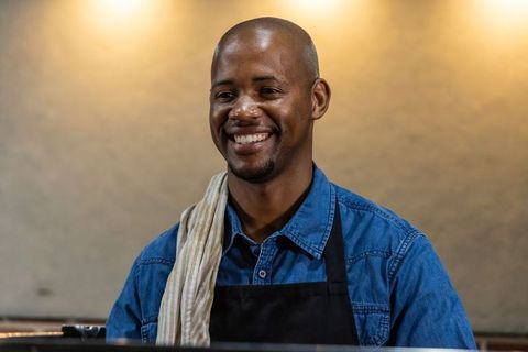 Smiling african barista serving coffee behind counter in cozy cafe interior