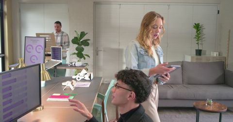 Diverse team collaborating with tablet, monitor and tabletop robots in modern coworkspace