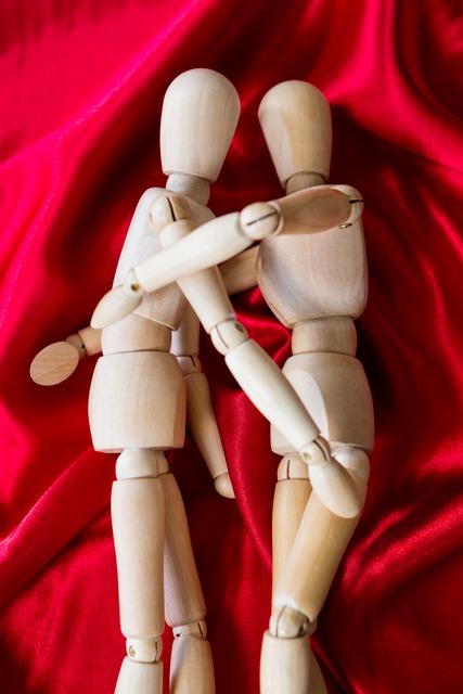 Wooden figurines embracing on vibrant red fabric, symbolizing love and intimacy. Ideal for use in art projects, relationship counseling materials, romantic greeting cards, and conceptual artwork.