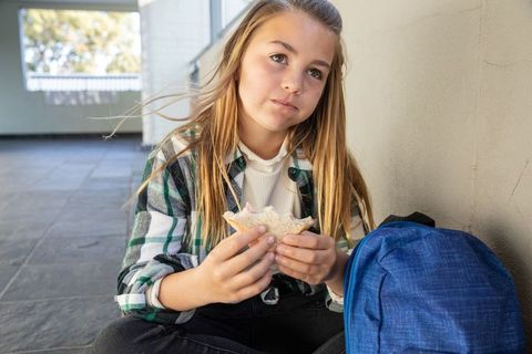 Girl Eating Sandwich Near Window with Backpack