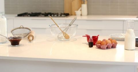 Bright modern kitchen countertop with glass mixing bowl, whisk, eggs, milk, baking prep
