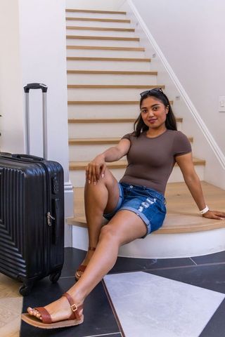 African woman sitting on staircase holding carry-on suitcase preparing for travel