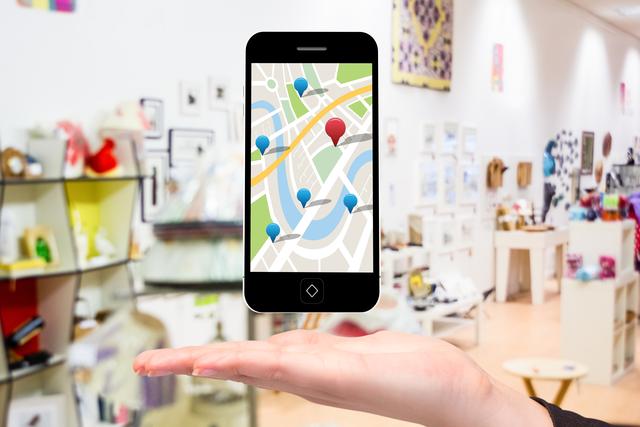 Hand holding smartphone displaying map app with several location pins, set in a modern store background. Ideal for illustrating digital navigation, mobile app functionality, and technology in retail environments. Perfect for use in advertisements for navigation apps, retail technology solutions, or modern shopping experiences.