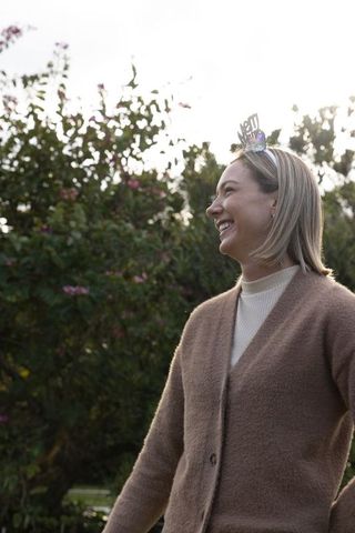Laughing woman wearing sparkly tiara in backlit backyard garden casual cardigan portrait