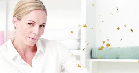Calm professional woman in white shirt sitting by linen shelves with gold confetti accents