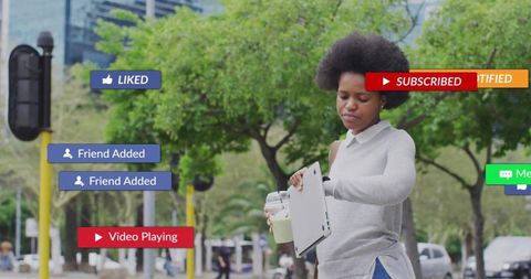 Young woman holding laptop and checking social notifications while walking urban boulevard