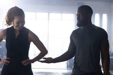 Mixed-race fitness partners offering hand in sunlit gym, coaching teamwork and motivation