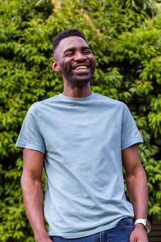 African american man smiling standing in garden wearing light blue t-shirt and watch