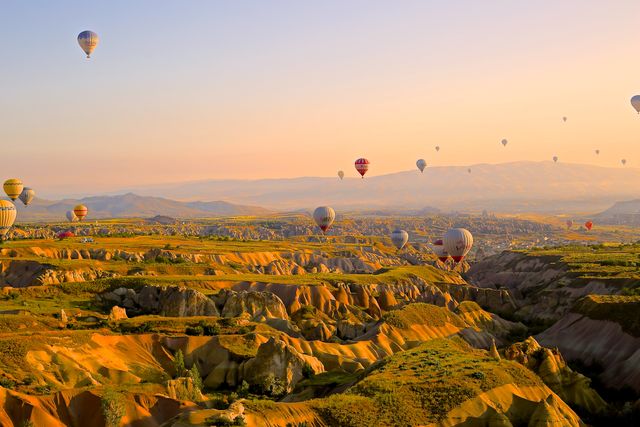 Balloons drifting over a rugged, otherworldly landscape with the horizon bathed in morning light. Ideal for travel agencies promoting exotic destinations, adventure tourism brochures, or websites focusing on unique and scenic experiences. Can also complement inspirational travel articles or decorative posters highlighting bucket list destinations.