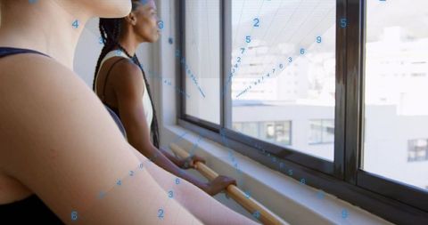 Holding barre: two women practicing ballet by studio windows with urban skyline