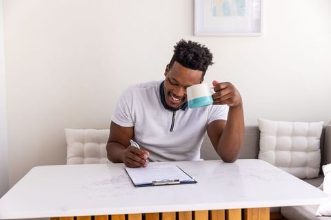 African American Man Writing on Clipboard While Enjoying Morning Coffee in Cozy Living Nook