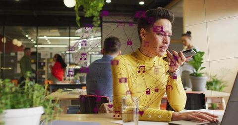 Worker speaking into smartphone while multitasking on laptop in modern coworking space