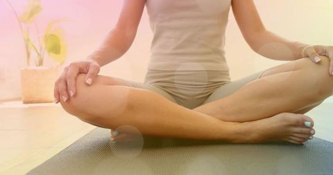 Woman meditating cross-legged on dark yoga mat in sunlit minimalist home for wellness