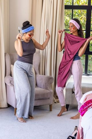 Multicultural friends enjoying pamper night, trying on maroon dress and dancing