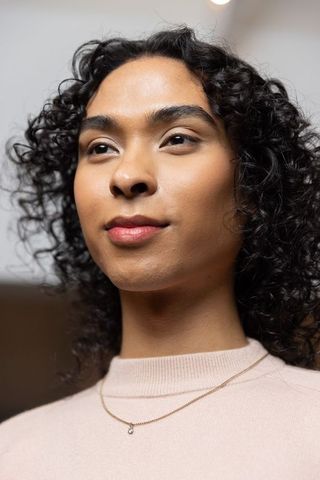 Confident non-binary person wearing pale pink sweater and gold pendant closeup portrait