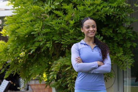 African american woman in activewear standing with arms crossed smiling by lush garden planter