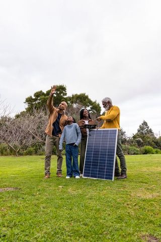 African american family inspecting solar panel in backyard using tablet for renewable energy