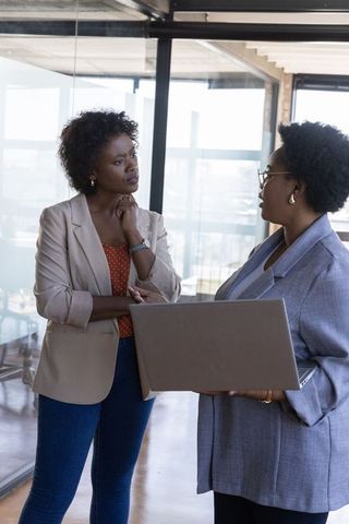 African American Female Colleagues Discussing Project in Office Hallway