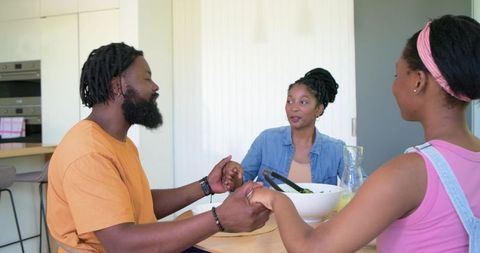 African family holding hands and sharing conversation at sunlit modern kitchen table