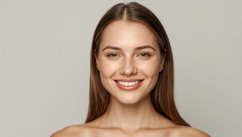 Smiling young woman headshot showing bare shoulders natural makeup soft studio lighting