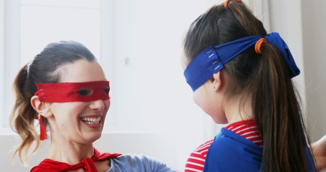 Happy caucasian mother and daughter in superhero masks and capes playing in sunny room. Fun, playing, dressing up, childhood, motherhood, togetherness, free time and domestic life, unaltered.