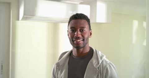Mid-adult african american man smiling in bright modern kitchen wearing gray hoodie