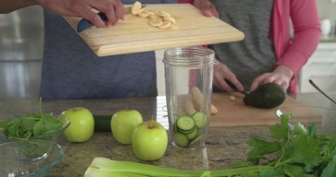 Couple preparing green smoothie with apples cucumber banana avocado in bright home kitchen