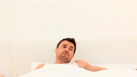 Man Slowly Waking Up in Casual Bedroom Setting