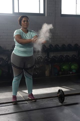 African american woman preparing heavy barbell lift with chalk dust in industrial gym