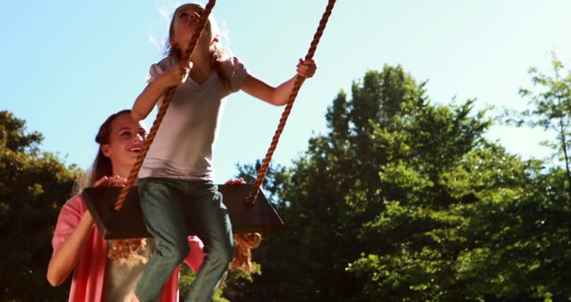 Little girl being pushed on a swing by her mother in the park on a sunny day - Download Free Stock Photos Pikwizard.com