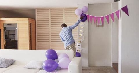 African American man decorating livingroom with purple balloons and bunting for party