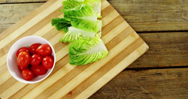 Fresh cherry tomatoes are placed beside crisp lettuce leaves on a wooden cutting board, with copy space. Ideal for content related to healthy eating, vegetarian diets, or meal preparation.