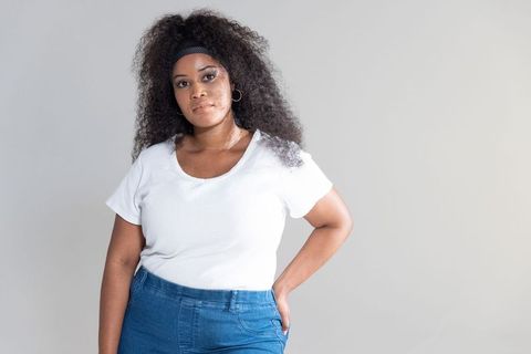 Confident african american woman posing in white ribbed tee and high-waist blue jeans