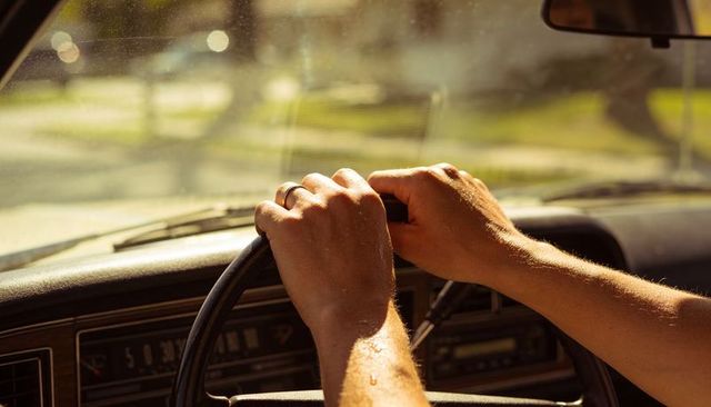 Gripping hands steering vintage car during golden hour drive showing wedding ring