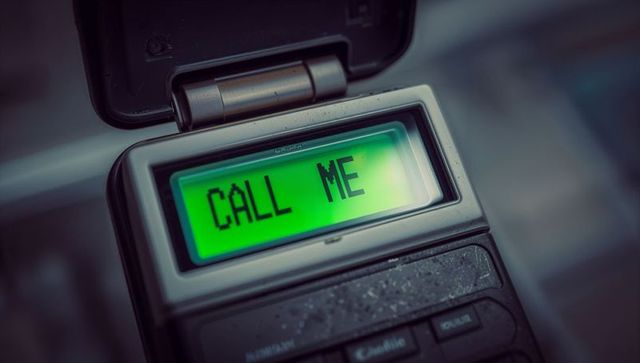 Retro flip phone displaying call me on green screen, dusty keypad macro, tech message