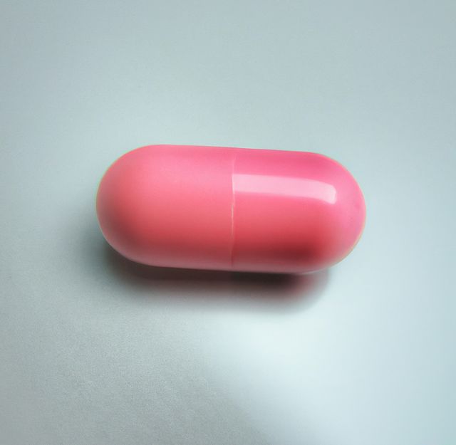Close up of one pink pill laying on white background. Medicine, healthcare and treatment concept.