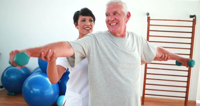 Happy physiotherapist helping elderly patient lift hand weights at the rehabilitation center 