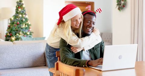 Diverse couple embracing during christmas with laptop
