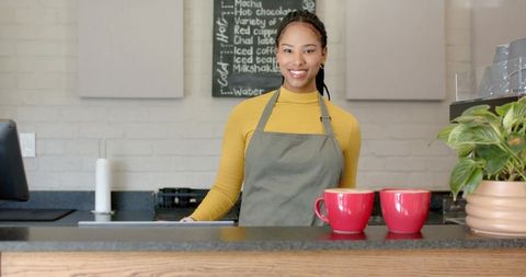 Smiling african american barista serving coffee at counter with red cups and chalkboard menu
