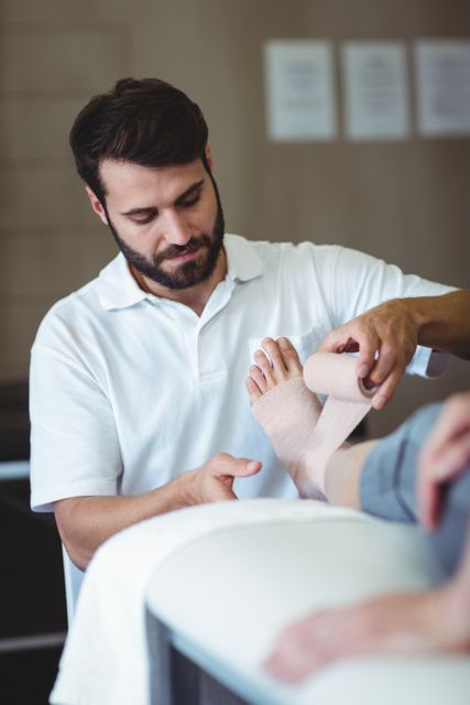 Physiotherapist bandaging an injured foot in a clinic, focusing on patient care and rehabilitation. Ideal for use in healthcare, medical, and rehabilitation contexts to illustrate professional treatment and therapy services.