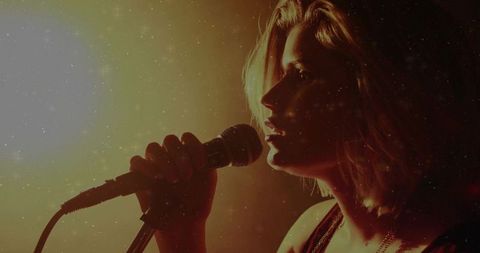Female Singer Performing in Amber Stage Lights Holding Wired Microphone Close-Up Vintage Grain