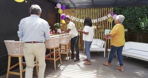 Multigenerational family celebrating birthday on backyard patio with balloons and gifts