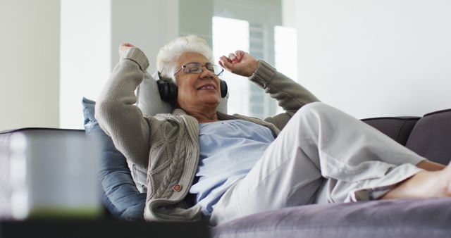 African american senior woman wearing headphones listening to music sitting on the couch at home. retirement senior lifestyle living in quarantine lockdown concept