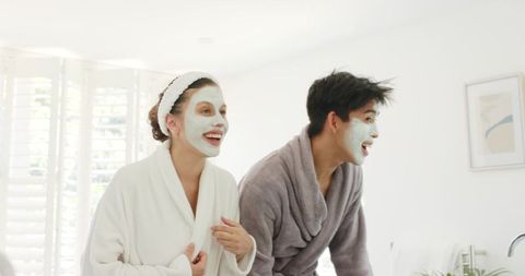 Diverse couple enjoying at-home facial ritual laughing together in bright spa bathroom