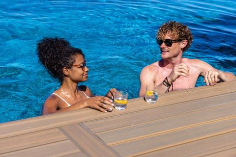 Mixed race couple relaxing in pool with lemon drinks wearing sunglasses at resort