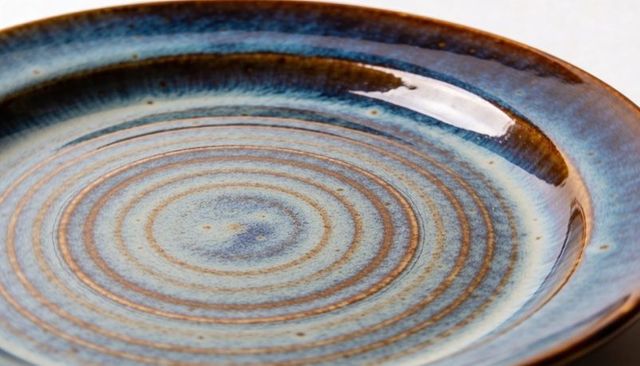 Handcrafted blue-brown ceramic plate with concentric rings and speckled glaze