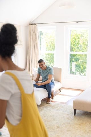 Young couple relaxing in sunlit living room reading mail and laughing on daybed with vaulted ceiling