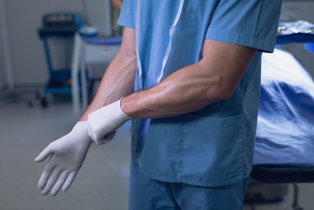 Image shows a male surgeon putting on surgical gloves, focusing on the preparation before surgery in a hospital operating room. Can be used in medical, healthcare, and hospital-related content to emphasize preparation and professionalism.