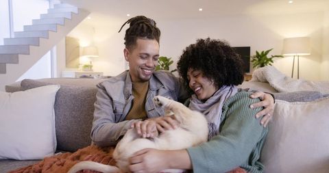 Happy couple laughing on sofa cuddling dog in cozy modern living room