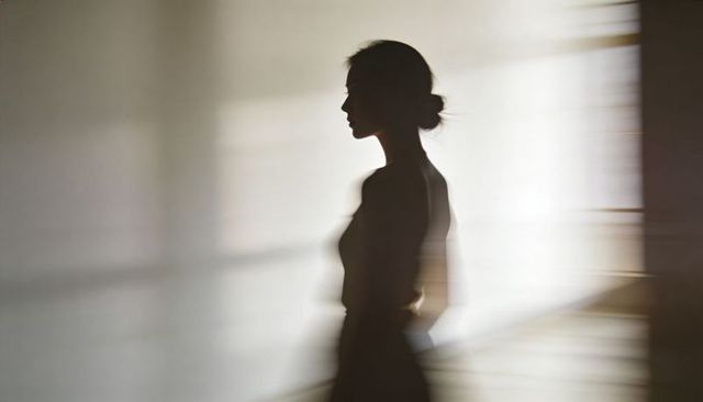 Silhouetted woman standing in sunlit room with blurred motion and window shadows
